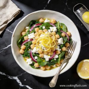 Beautifully plated high protein chickpea and spinach salad with lemon zest on black marble countertop